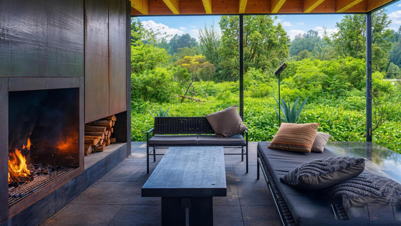 Outdoor living room of sustainable prefabricated home with fireplace and floor-to-ceiling windows, eco-friendly modular house patio space